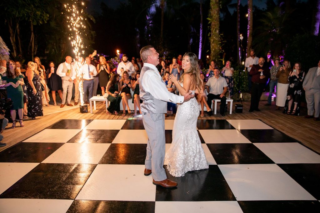 couple dancing at their wedding on black and white checkered dance floor with sparklers in the background